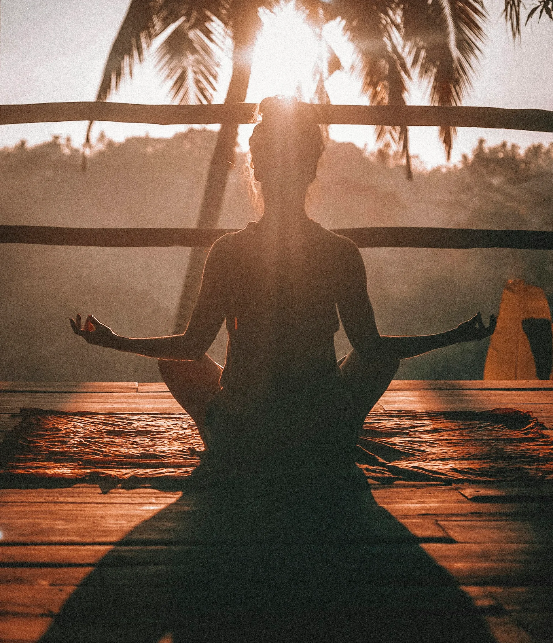 A person seated cross-legged in a meditation pose, silhouetted against a sunrise